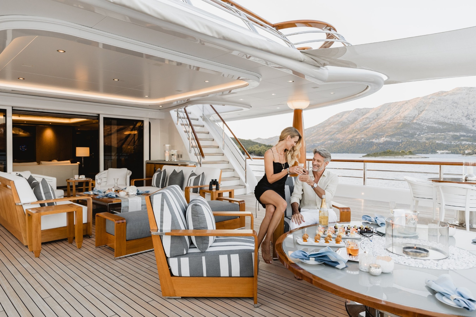 Couple enjoying sunset drinks on yacht deck with French Riviera coastline